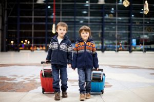 Children in holiday sweaters pulling suitcases at an airport.